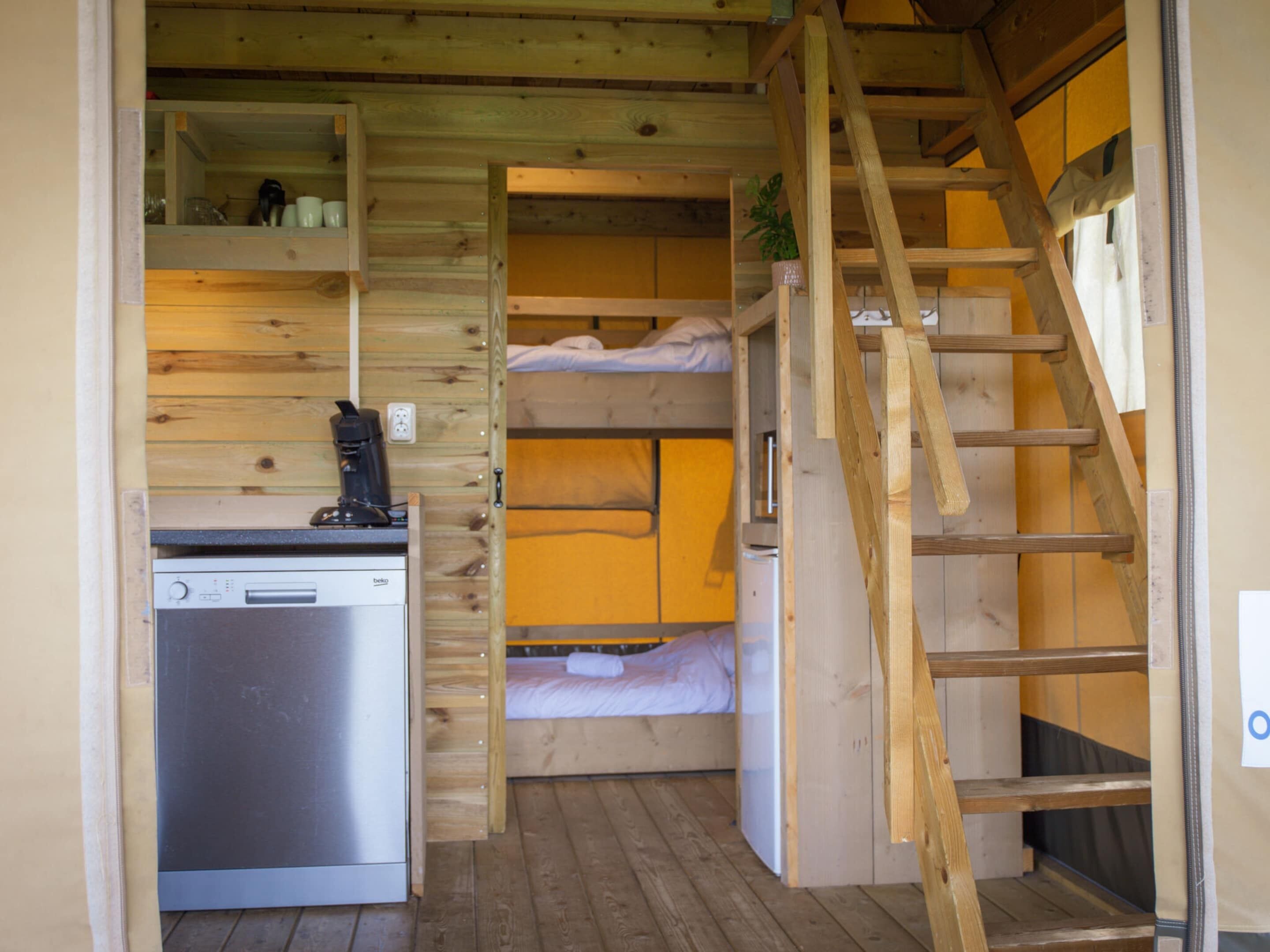 A compact room with a kitchenette, a bunk bed, and a wooden staircase.