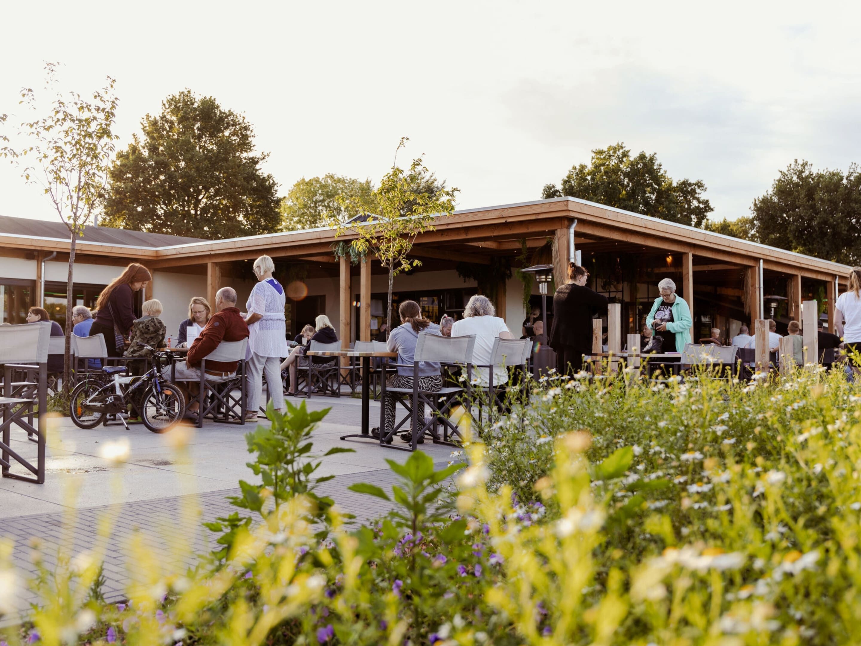 An outdoor seating area with tables and chairs, surrounded by greenery and flowers.