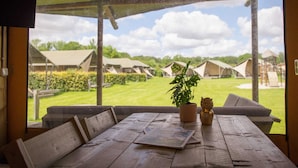 A wooden table with a plant and a decorative item, overlooking a grassy area with tents. - Well Furnished Tent Lodge with Terrace near Veluwe (Voorthuizen)