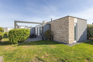 A modern building with a brick facade, a flat roof, and a patio area with outdoor furniture. - Single Storey Lodge With Dishwasher, Near the Beach (Callantsoog)