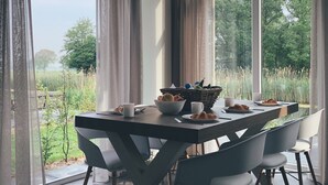 Een eetgedeelte met een tafel voor vier personen, omringd door stoelen, met uitzicht op een grasveld door grote ramen.