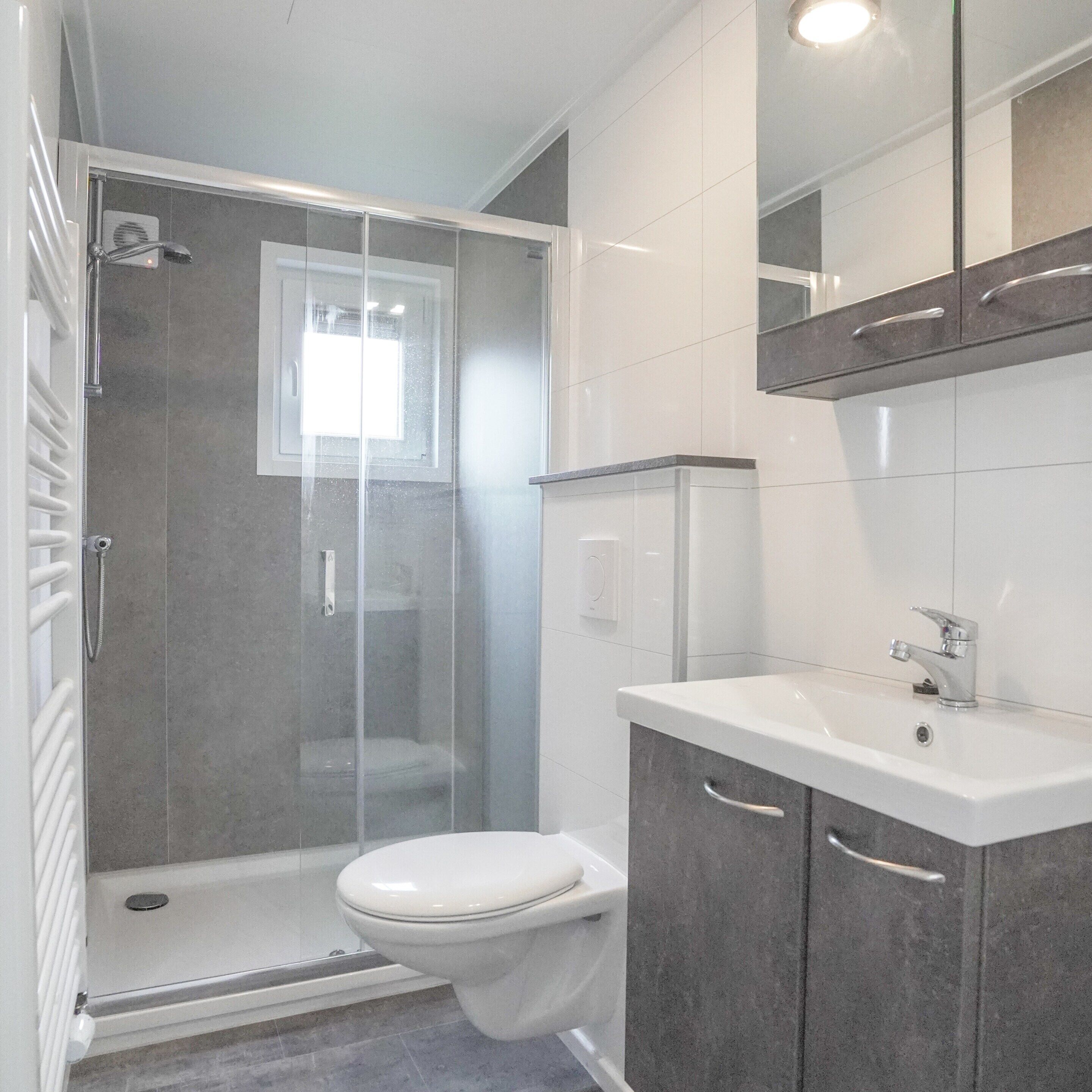 Une salle de bain moderne avec une douche à l’italienne, des toilettes, un lavabo et un miroir au-dessus du lavabo.