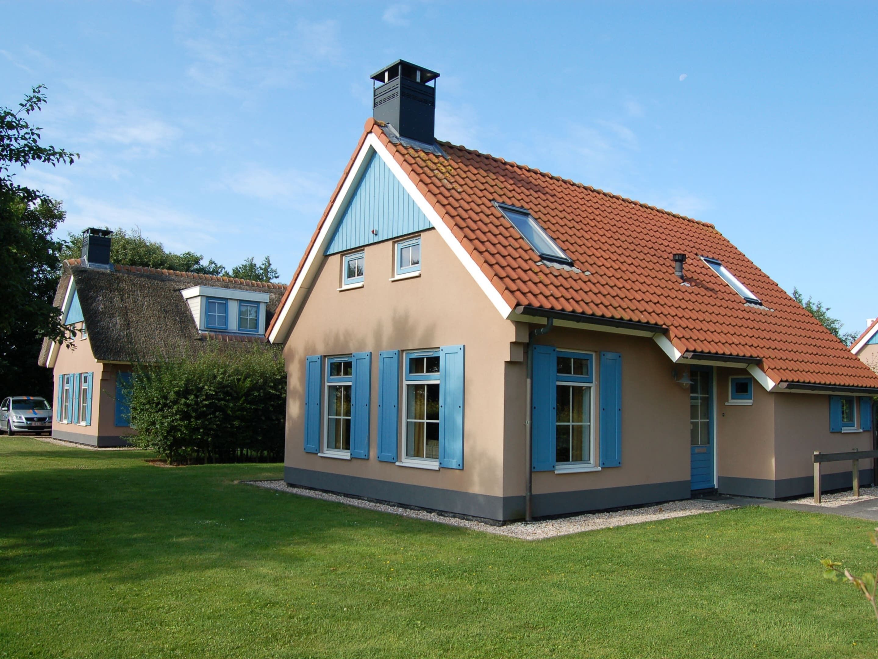 Ein zweistöckiges Haus mit rotem Ziegeldach, blauen Fensterläden und einem Schornstein.