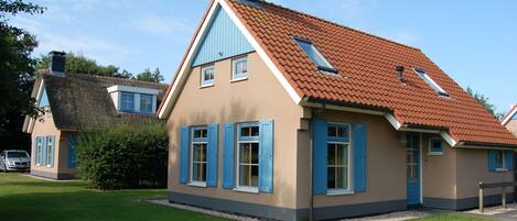Ein zweistöckiges Haus mit rotem Ziegeldach, blauen Fensterläden und einem Schornstein.