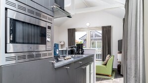 A modern kitchen with a built-in microwave, stove, and sink. There is a green sofa and a window with curtains in the background. - Cozy Chalet Right on the Water in Friesland (Akkrum)