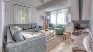 Ein modernes Wohnzimmer mit grauem Sofa, einem kleinen Couchtisch, einem grünen Sessel und einem Kamin.