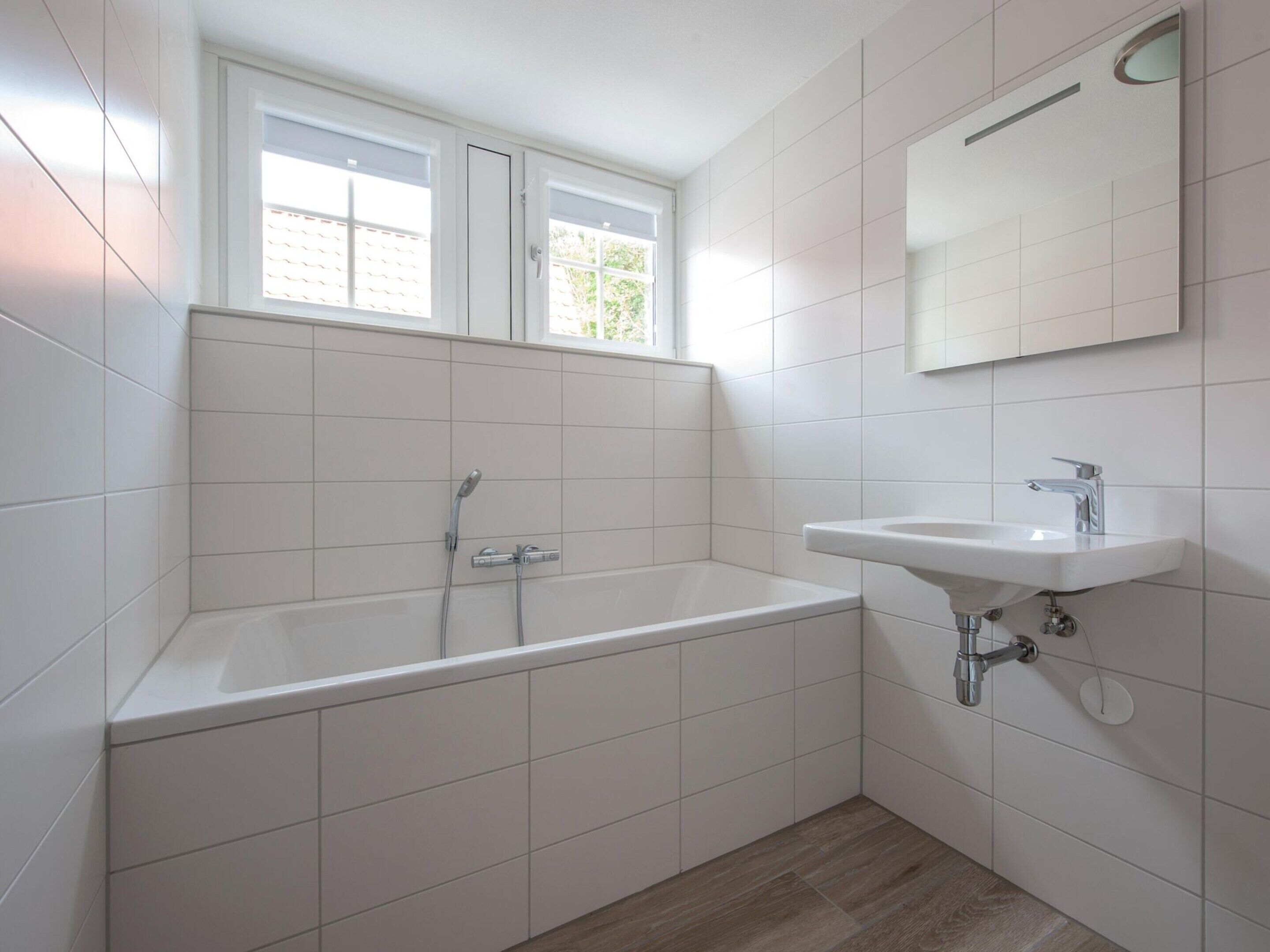 Et moderne badeværelse med badekar, vask og et vindue over karret.