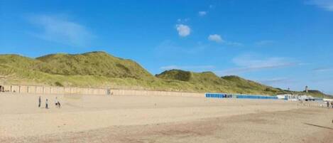 A sandy beach with a few people, a blue fence, and green hills in the background.