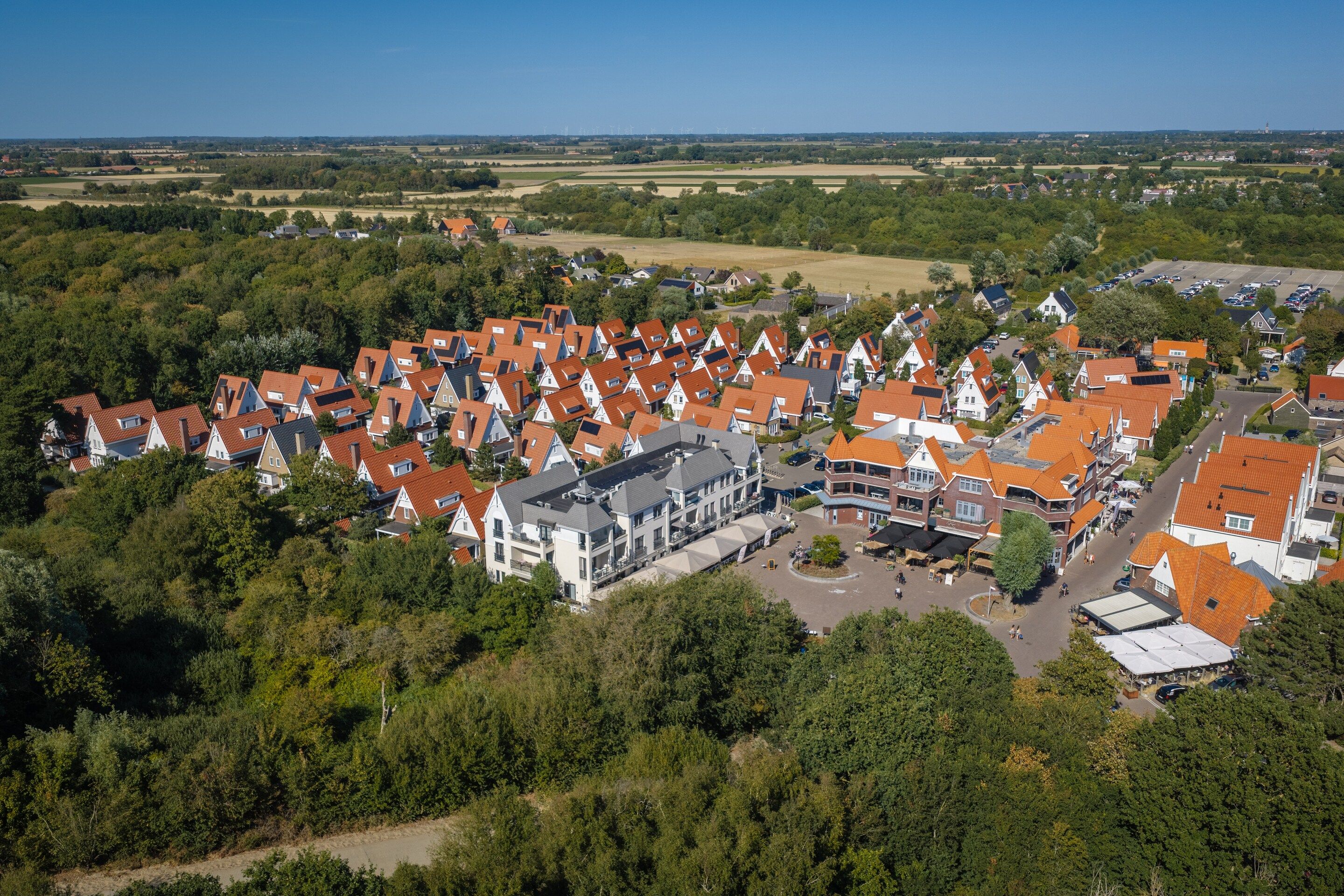 An aerial view of a residential area with houses featuring red-tiled roofs, surrounded by greenery and open fields.