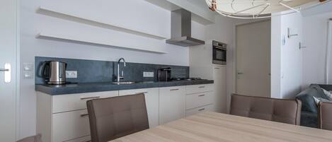 A modern kitchen with a dining area, featuring a wooden table, chairs, a coffee maker, and a built-in oven.