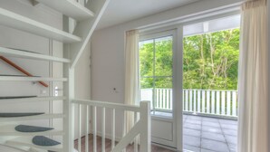 Eine Treppe mit weißen Geländern führt zu einem Balkon mit Blick auf Bäume.