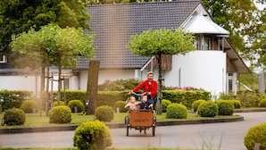 A person in a red jacket pushing a cart with two children. - Beautiful House With Garden (Hellendoorn)