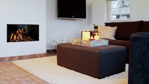 A living room with a fireplace, a flat-screen TV mounted on the wall, a brown sofa, and a window with a yellow blind. - Beautiful House With Garden (Hellendoorn)