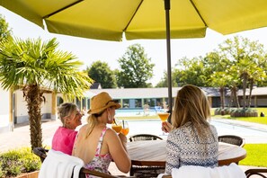 Three people seated at an outdoor table with a yellow umbrella, overlooking a swimming pool and greenery. - Beautiful House With Garden (Hellendoorn)