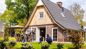 A wooden house with a sloped roof, a front porch, and a garden with small plants. - Family Villa + Sauna & Sunroom (Hellendoorn)