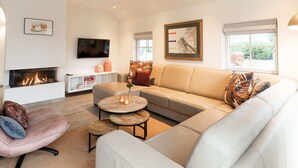 A modern living room with a fireplace, a sofa, a coffee table, and a TV mounted on the wall. - Family Villa + Sauna & Sunroom (Hellendoorn)