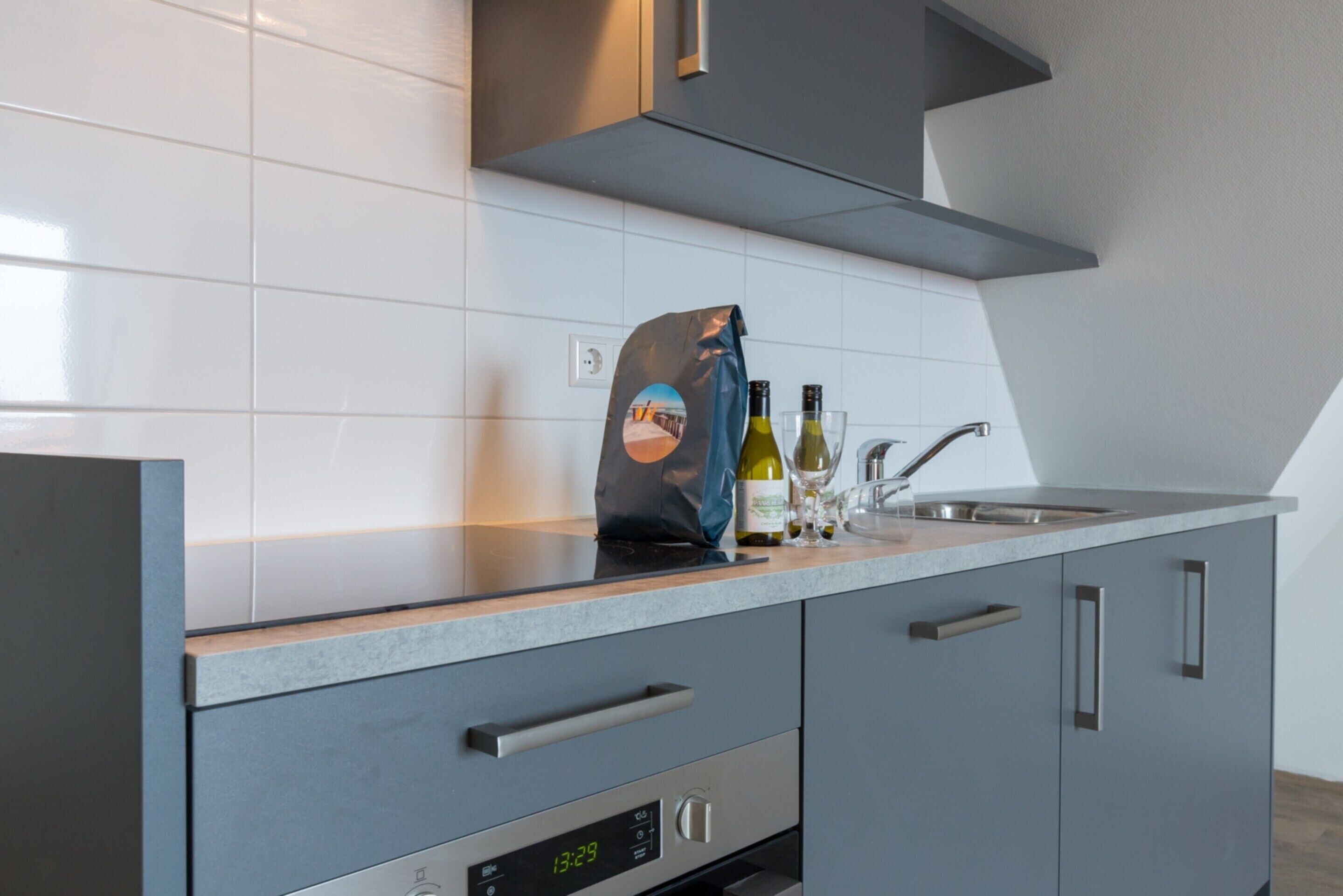 A modern kitchen with a digital clock, stainless steel appliances, and a bag of groceries on the counter.