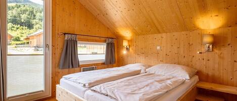 Une chambre dans une cabane en bois, avec deux lits, une fenêtre avec des rideaux et une vue sur une zone boisée.