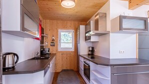 Kompakti keittiö, jossa on modernit kodinkoneet, puuseinät ja pieni ikkuna.