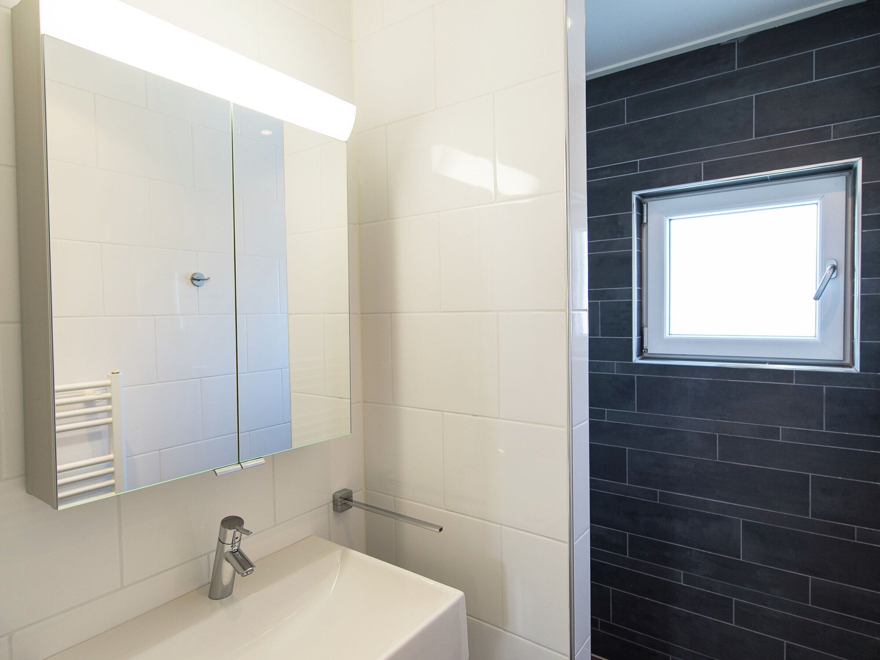 Een badkamer met een witte wastafel, een spiegel en een raam.