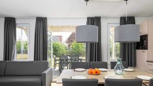 A modern living room with a sofa, dining table, chairs, and a kitchen area with a microwave. - Villa in Arcen With Free Thermal Bath Access (Arcen)