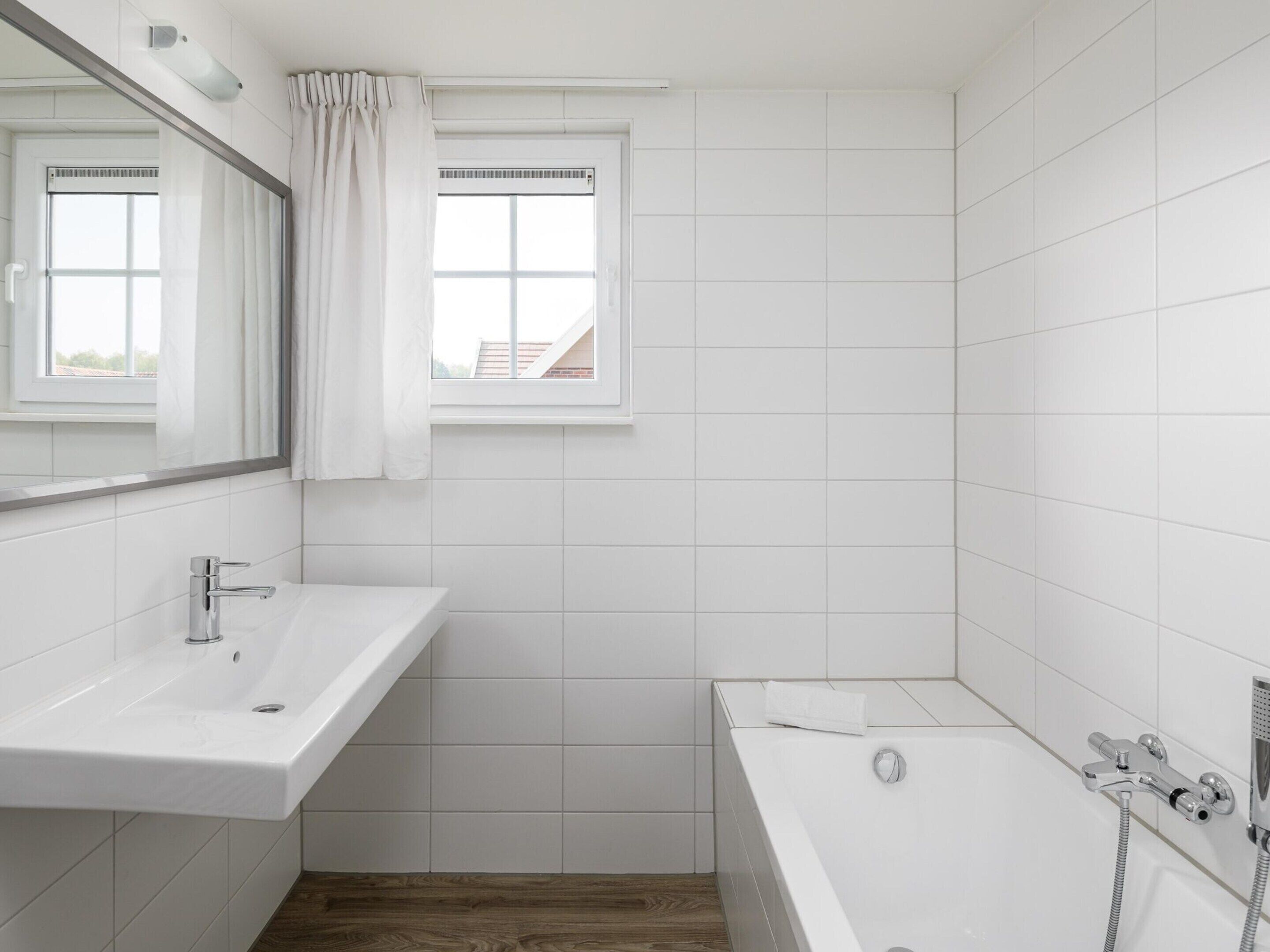 A modern bathroom with a white sink, a bathtub, and a window with curtains.