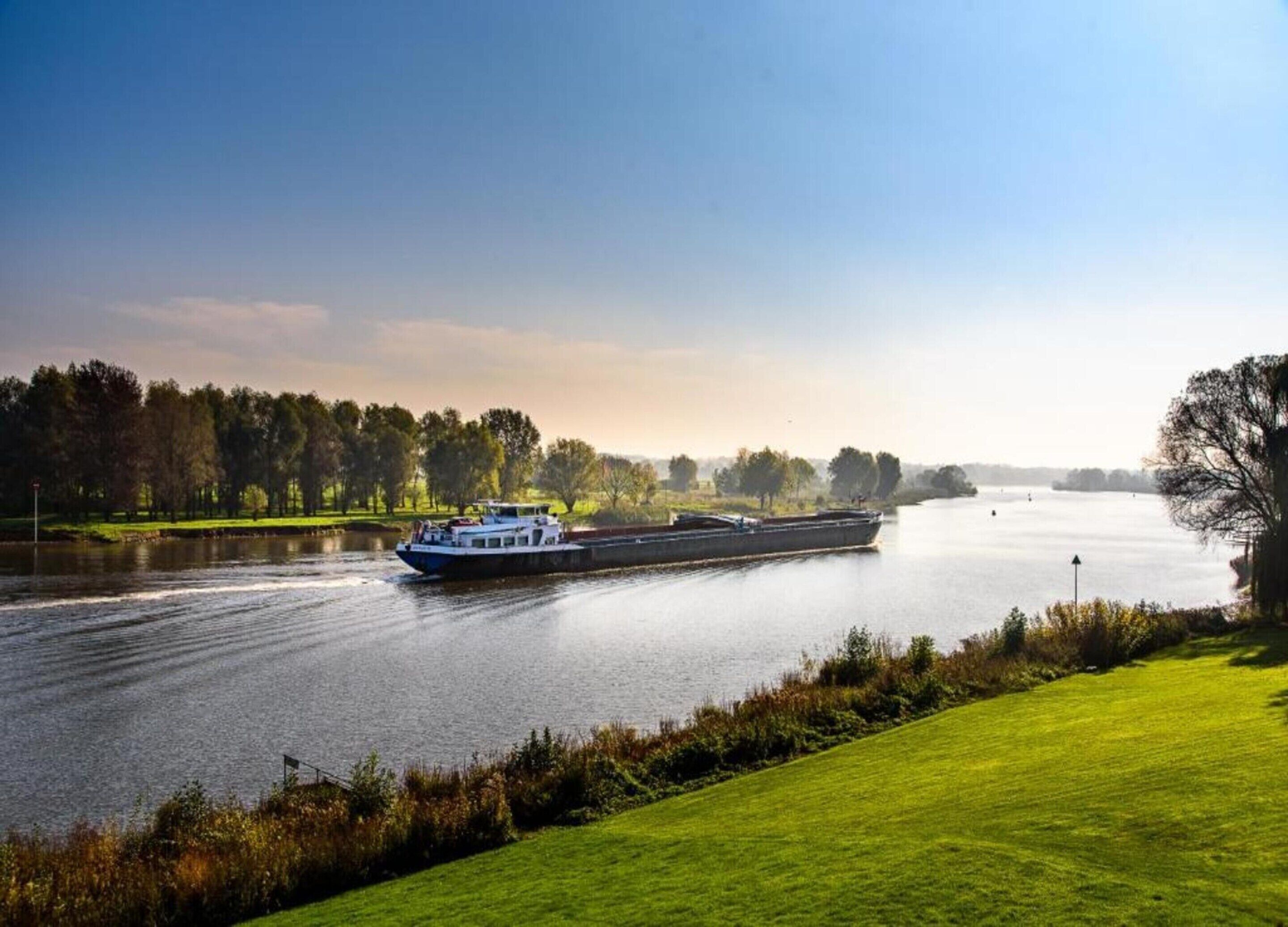 A river with a boat, grassy banks, and trees in the background.