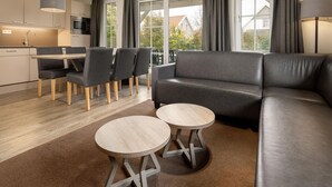 A modern living room with a grey sofa, two round tables, and a dining area with chairs. - Villa in Arcen With Free Thermal Bath Access (Arcen)