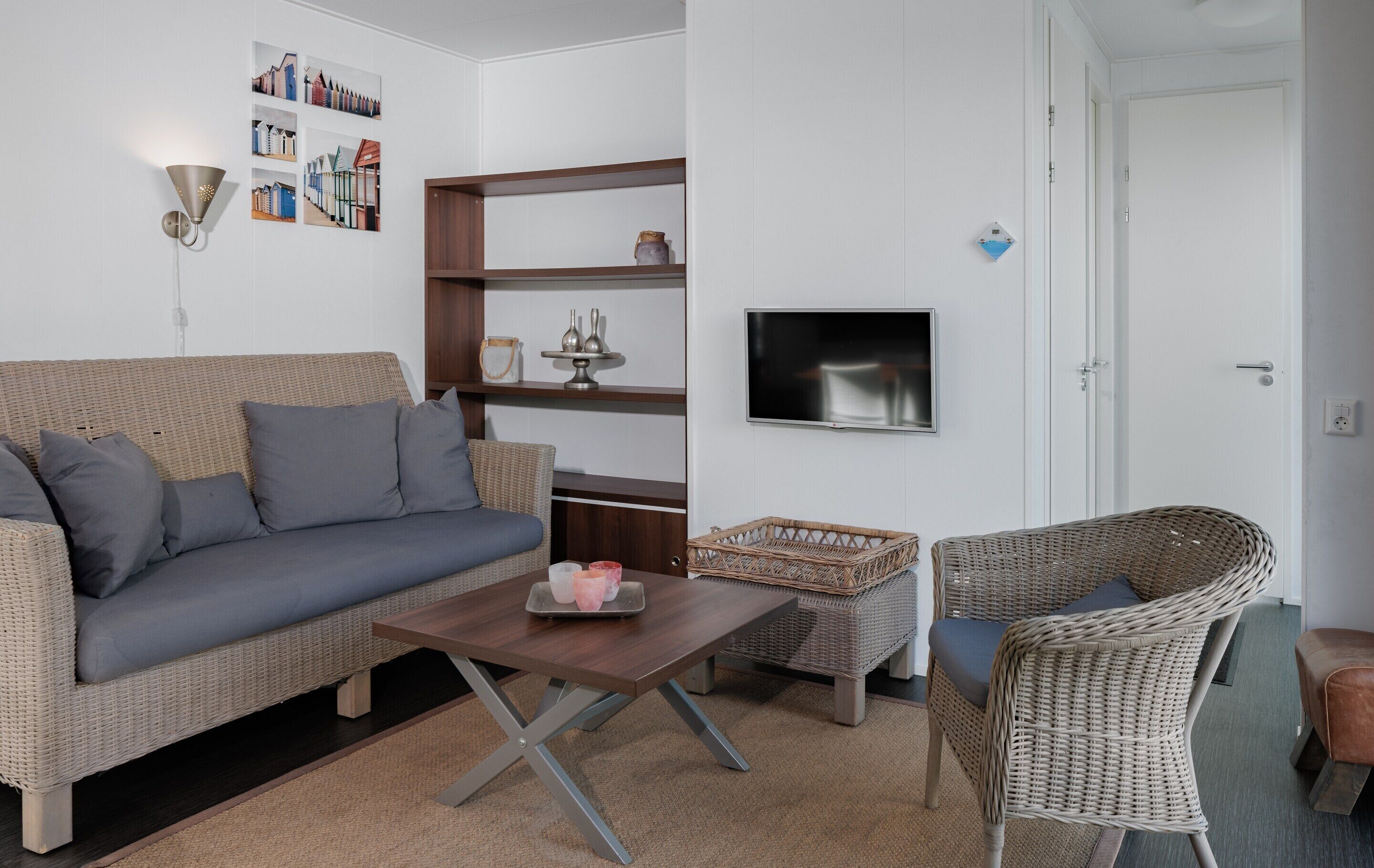 A living room with a sofa, a coffee table, wicker furniture, a TV, and shelves with decorative items.