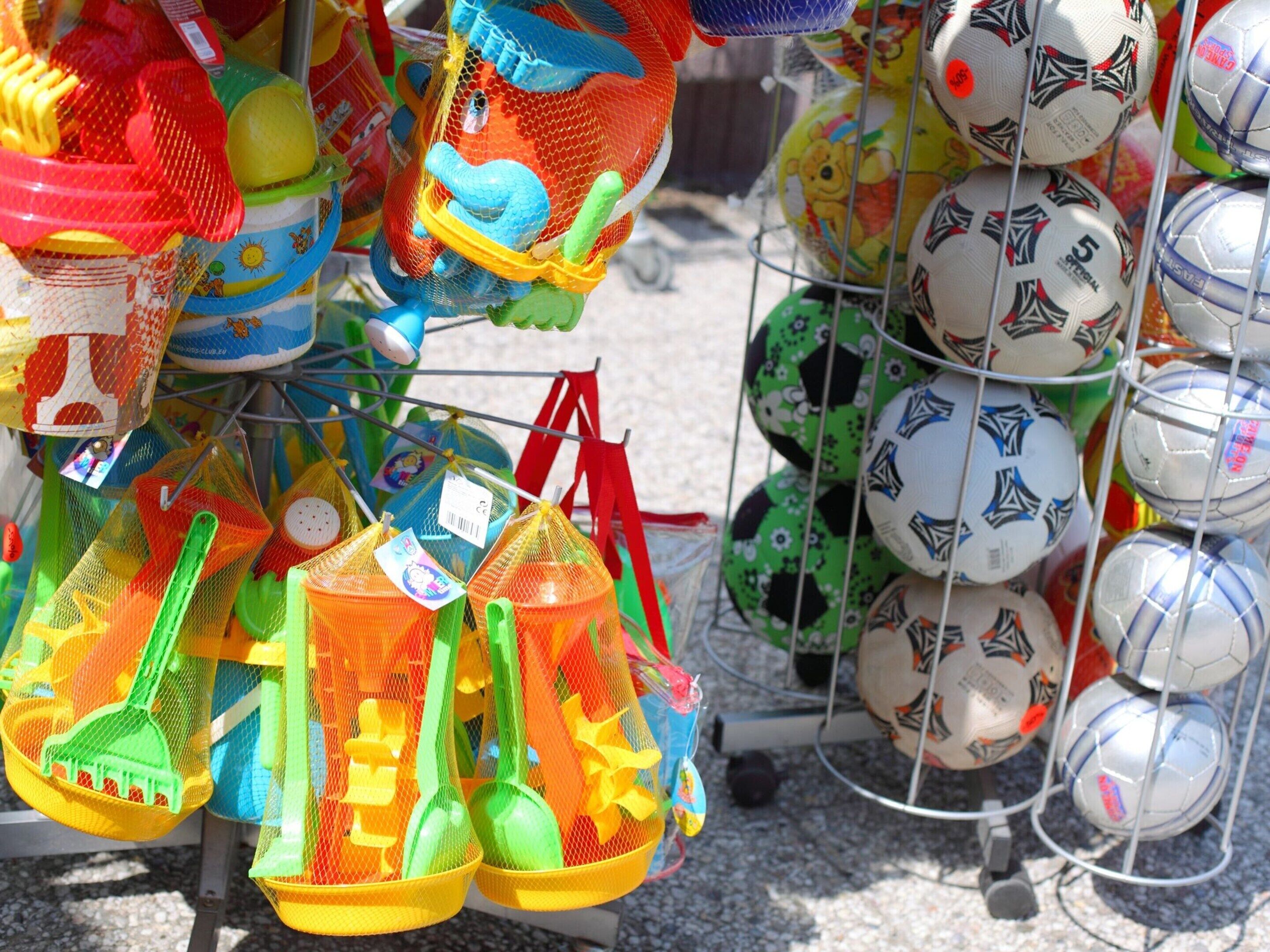 Una variedad de juguetes de playa coloridos y pelotas deportivas exhibidos en un estante.