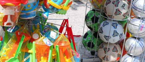 Una variedad de juguetes de playa coloridos y pelotas deportivas exhibidos en un estante.