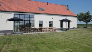 Un bâtiment doté d’un toit recouvert de tuiles rouges, de grandes fenêtres et d’un patio aménagé avec des tables et des chaises.