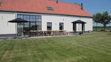 Een gebouw met een rode pannendak, grote ramen en een patio met tafels en stoelen.