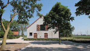 Un bâtiment blanc avec un toit rouge, des volets en bois et une allée gravillonnée.