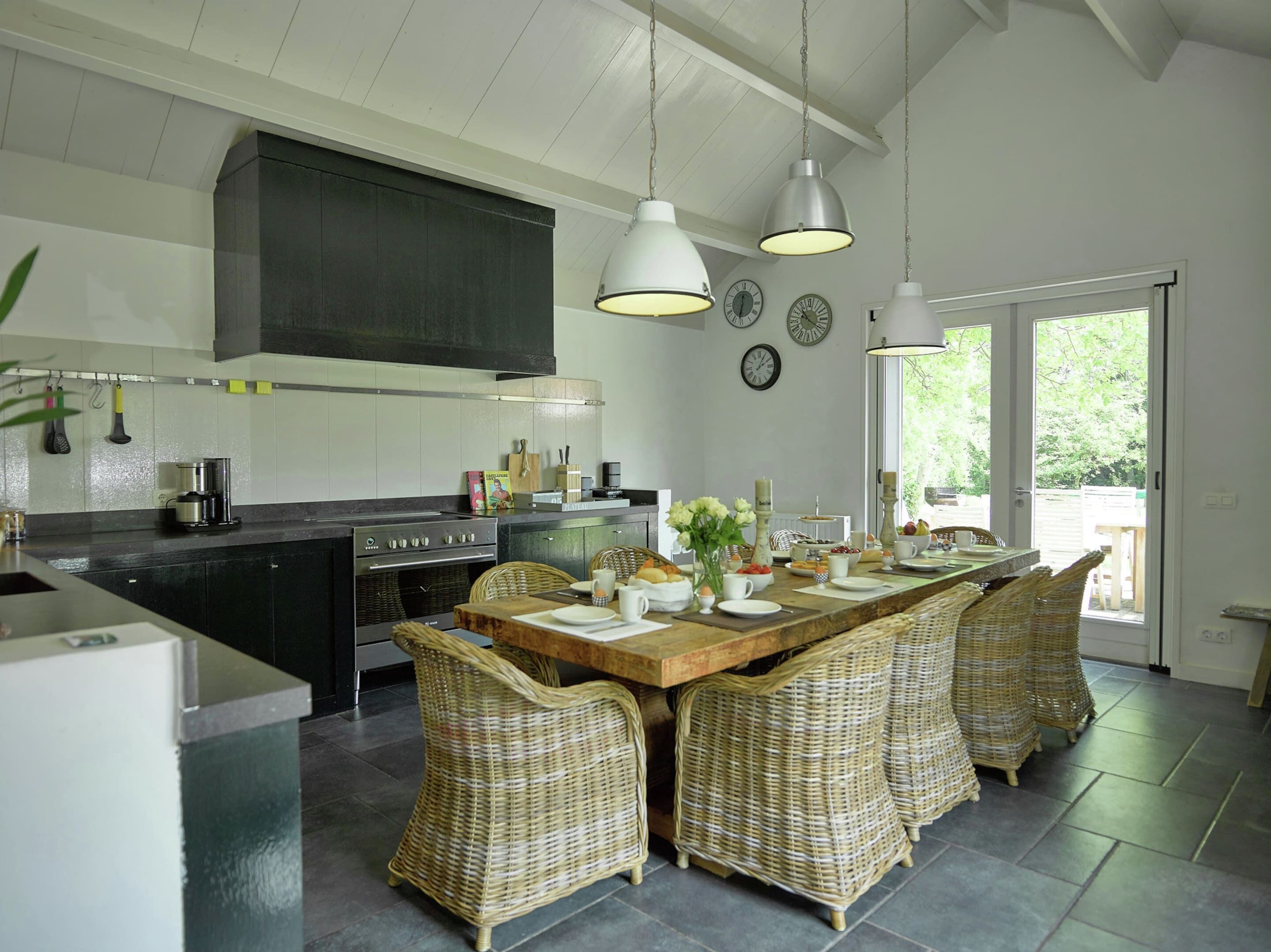 Een moderne keuken met een centraal eiland, een eethoek met rieten stoelen, en een groot raam dat voor natuurlijk licht zorgt.