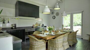 Een moderne keuken met een centraal eiland, een eethoek met rieten stoelen, en een groot raam dat voor natuurlijk licht zorgt.