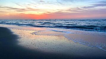 Een strand met golven en een ondergaande zon.