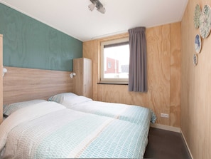 A bedroom with two beds, wooden headboard, a window with curtains, and a wall-mounted cabinet.