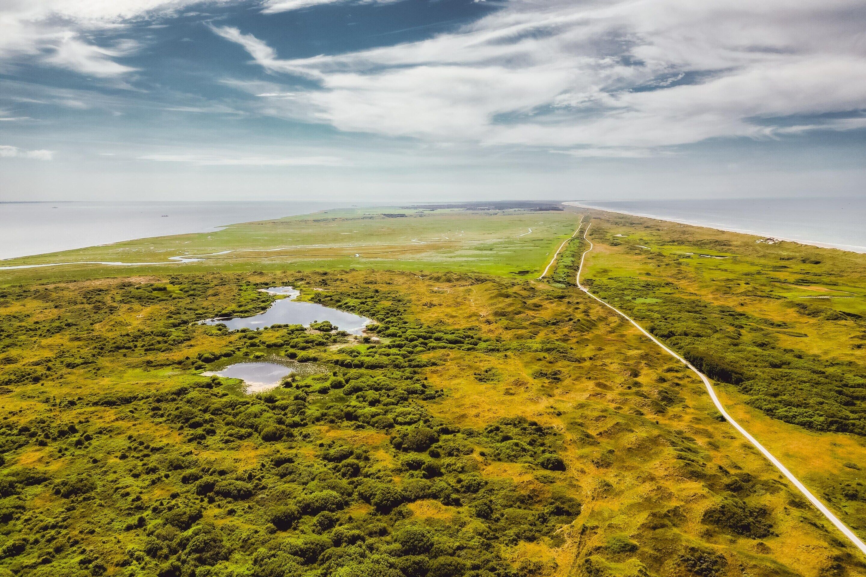 An aerial view of a coastal landscape with a road, green fields, and a body of water.