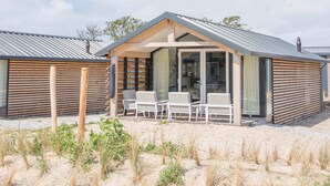 A modern beach house with a covered patio, outdoor seating, and a sandy landscape. - Ameland Lodge w/ Veranda (Hollum)