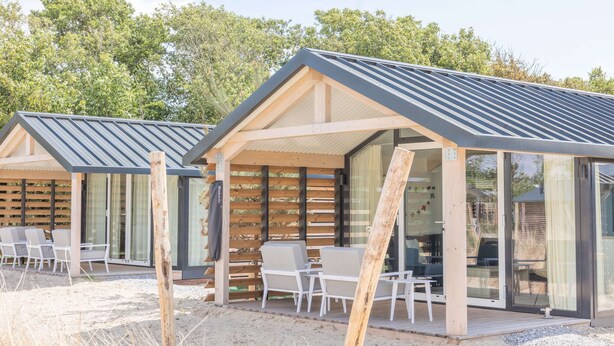 A modern outdoor seating area with wooden pergolas and glass doors, surrounded by natural vegetation. - Ameland Lodge w/ Veranda (Hollum)