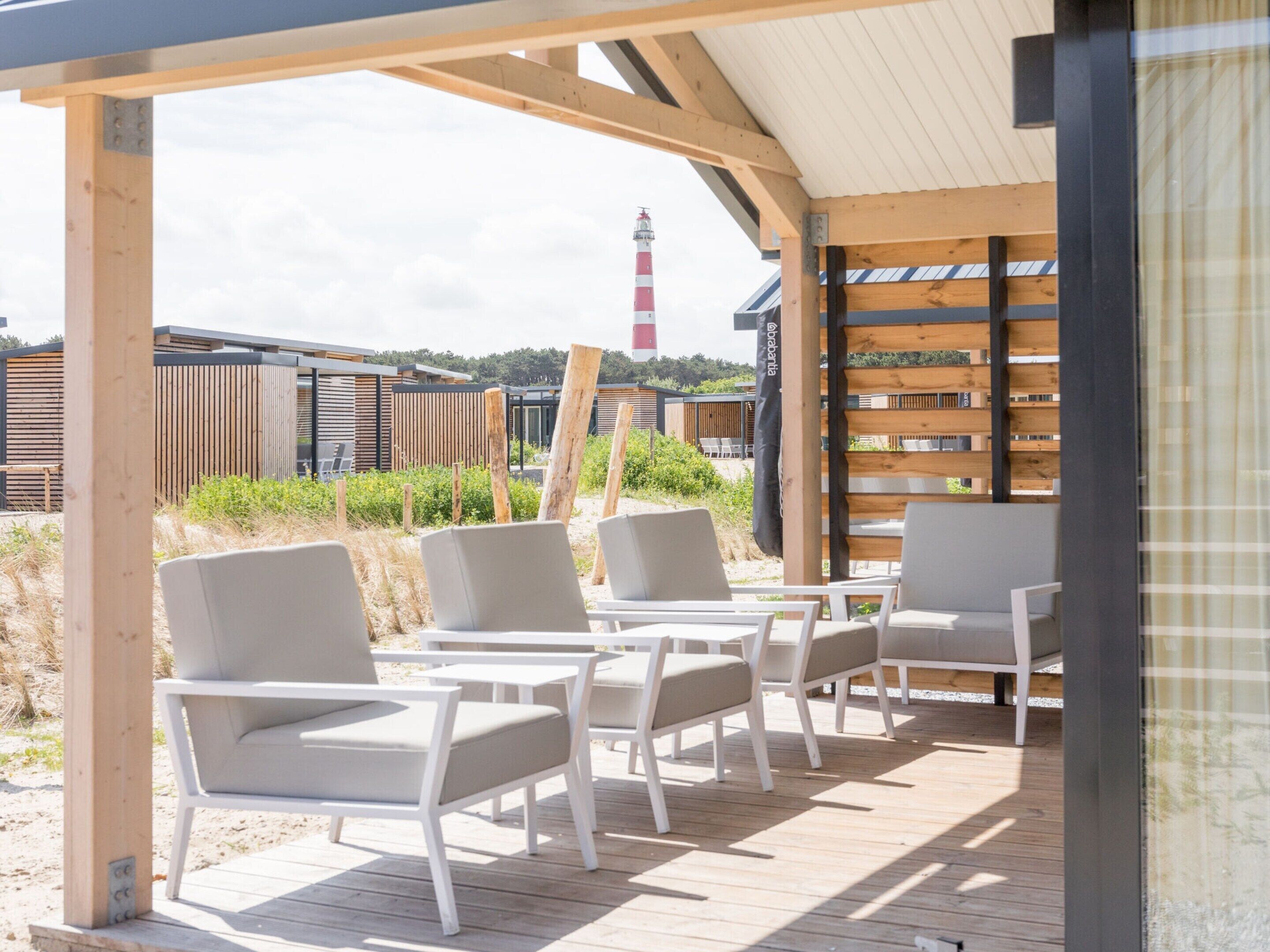 Un espace extérieur aménagé avec des sièges, protégé par un toit, comprenant des chaises blanches et une terrasse en bois.