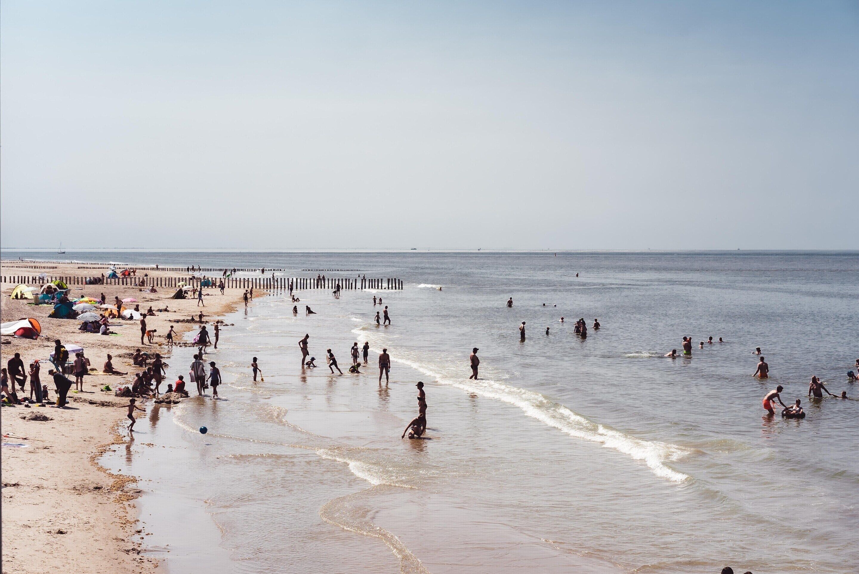 Een strand met mensen die zwemmen en over het strand lopen.