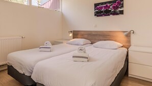 A hotel room with two beds, a radiator, a window with a view of trees, and a wall-mounted artwork.