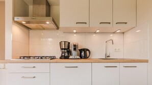 A modern kitchen with white cabinets, a gas stove, a coffee maker, and a kettle.