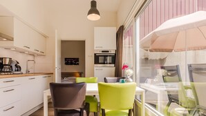 A modern kitchen with white cabinets, a dining area with green chairs, and a view of the outside through a large window.