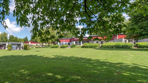 A residential area with multiple houses, a well-maintained lawn, and trees providing shade.
