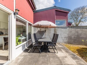 A patio with a table and chairs, a glass door leading to a kitchen, and a red building in the background.