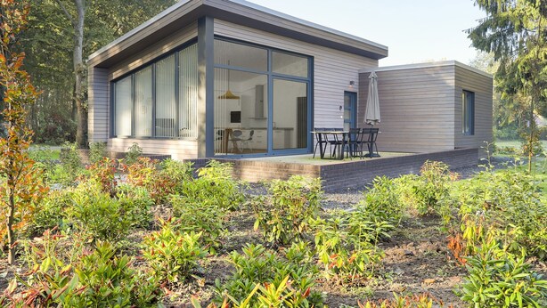 A modern house with large glass windows, a patio with outdoor furniture, and a garden with various plants. - Getaway With Covered Veranda (Enter)