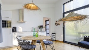 A modern kitchen with white cabinets, a round wooden table, and black chairs. There is a large window with a view of the outdoors. - Getaway With Covered Veranda (Enter)
